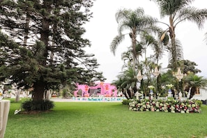 A stage with a pink backdrop, surrounded by palm trees and a flower arrangement. - w Spacious 12br Stay w Pool BBQ in Pachacamac (Pachacámac)