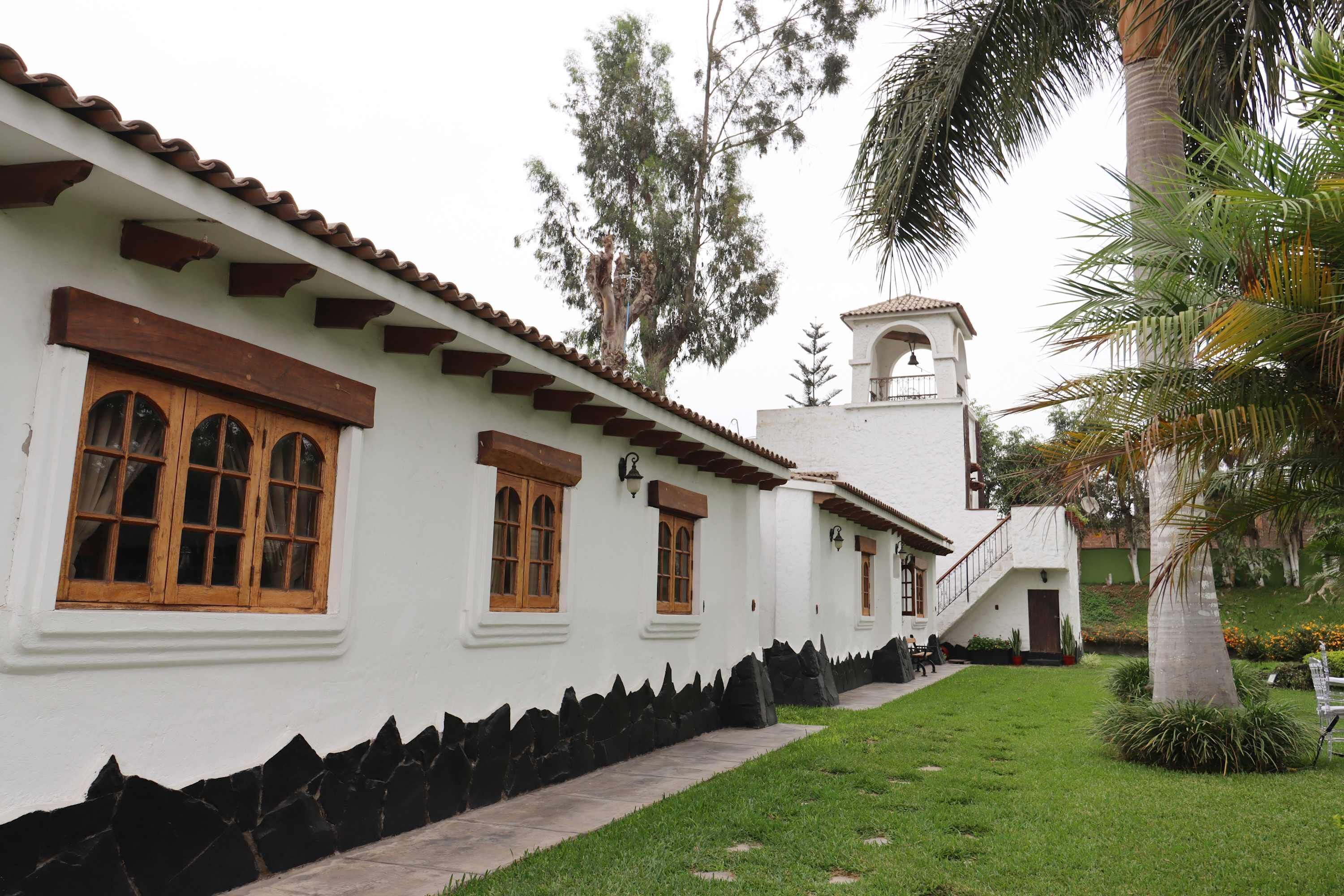 A white building with wooden window frames, a stone base, and a bell tower.