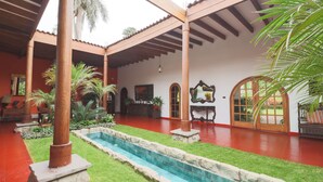 A courtyard with a swimming pool, palm trees, and a covered seating area. - w Spacious 12br Stay w Pool BBQ in Pachacamac (Pachacámac)
