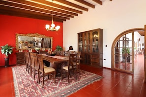 Uma sala de jantar com mesa e cadeiras de madeira, parede em vermelho, lustre e espelho grande.