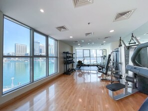 Ein Fitnessstudio mit großen Fenstern, Trainingsgeräten und Blick auf Stadt und Wasser.