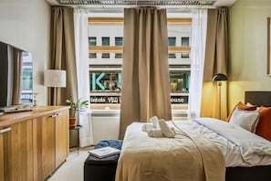 A hotel room with a bed, bedside table, lamp, and a view of the city through large windows. - 4BR in City Centre. Stockmann 50m. (Helsinki)