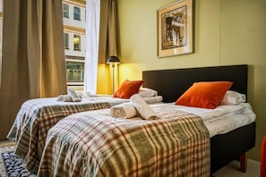 Ein Hotelzimmer mit zwei Betten, einem Kopfteil, einer Lampe, einem gerahmten Bild und einem Fenster mit Vorhängen.