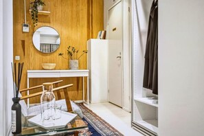 A compact room with a wooden wall, a round mirror, a white cabinet, a small table with a glass vase, and a door leading to a closet. - 4BR in City Centre. Stockmann 50m. (Helsinki)