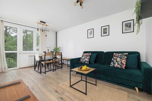 Ein modernes Wohnzimmer mit einem grünen Sofa, einem Holztisch und einem Essbereich mit Tisch und Stühlen.
