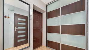 A hallway with a wooden door, a sliding glass door, and a light fixture on the wall. - Modern Studio on Piotrkowska Street City View (Łódź)
