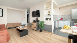 A modern living room with a sofa, a coffee table, a TV, a small kitchen area with a fridge, and a dining table with bananas. - Modern Studio on Piotrkowska Street City View (Łódź)