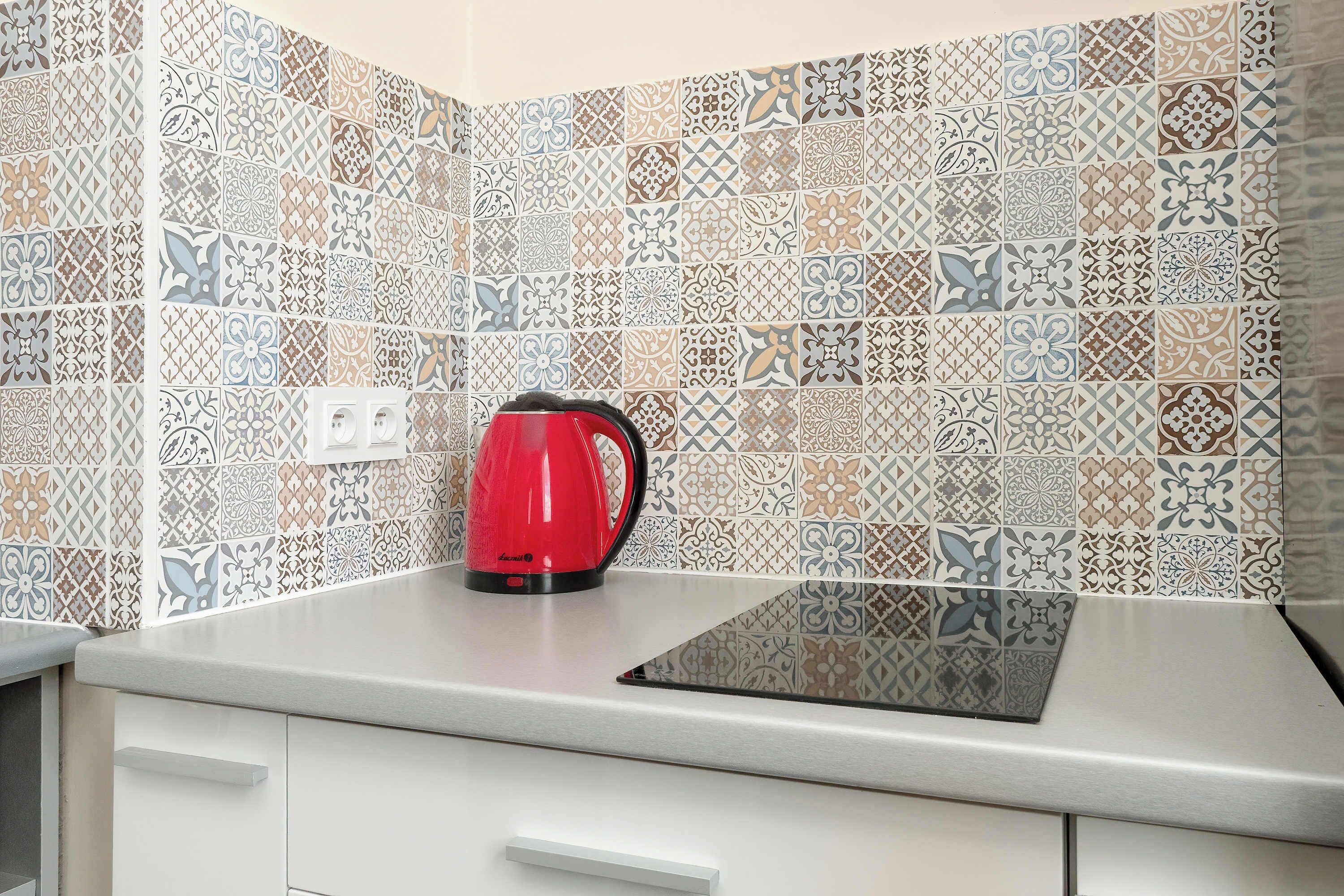 A kitchen with patterned tiles, a red kettle, and a modern countertop.