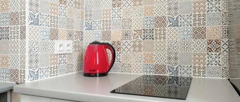 A kitchen with patterned tiles, a red kettle, and a modern countertop.