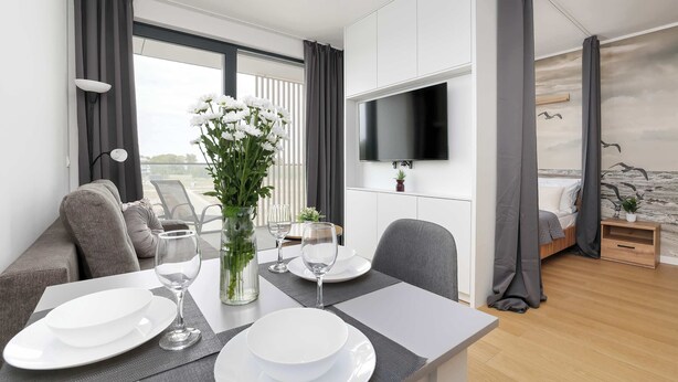Ett modernt hotellrum med en matplats, en TV som är monterad på väggen, en säng med gardiner och utsikt över omgivningarna.