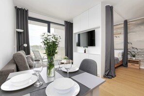 Habitación de hotel moderna con comedor, televisor montado en la pared, cama con cortinas y vistas al exterior.