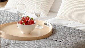 En säng med vita kuddar och ett brickbord med en skål jordgubbar och två glas.