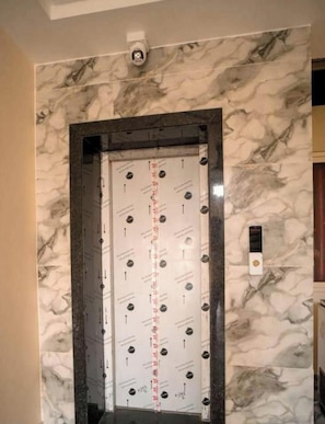 An elevator with a marble wall design, a visible scale, and a security camera above it. - Hotel Shree Karni Palace (Beawar)
