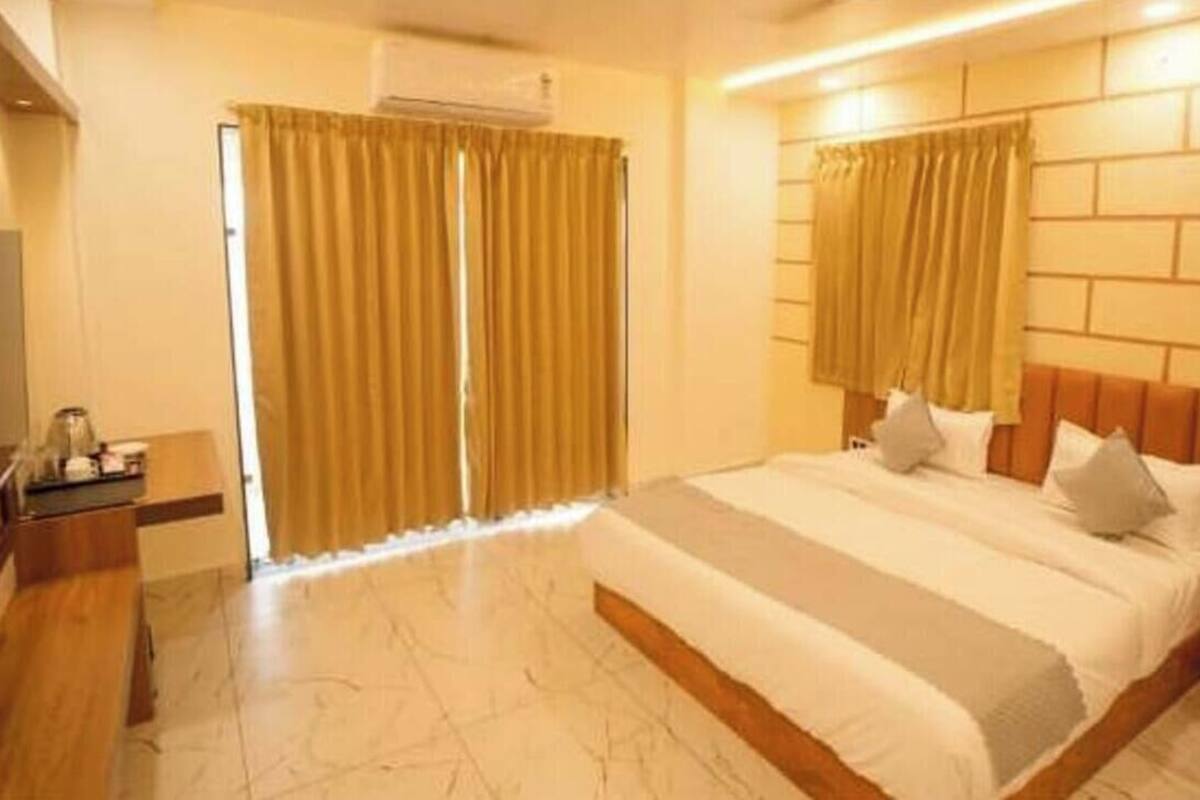 Habitación de hotel con una cama grande, cabecera de madera, mesita de noche y ventana con cortinas.