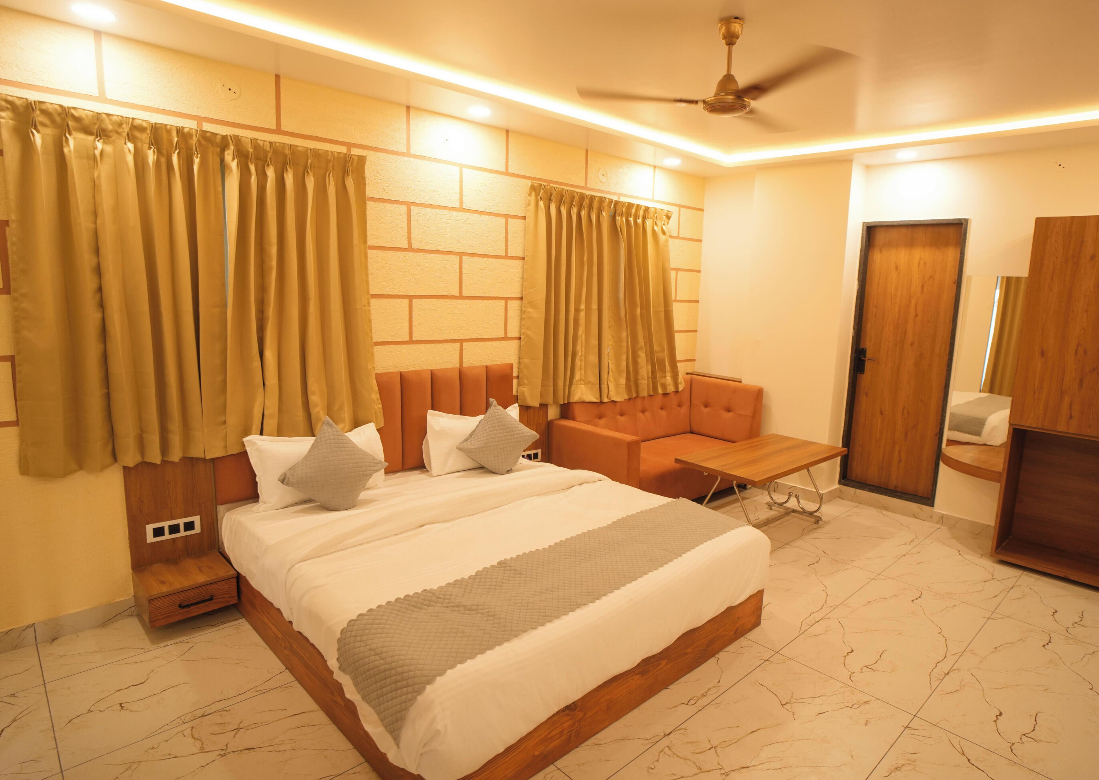A bedroom with a large bed, a sofa, a small table, a ceiling fan, and a wooden wardrobe.