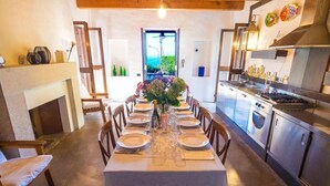 A dining area with a table set for six, a fireplace, and a kitchen with stainless steel appliances.