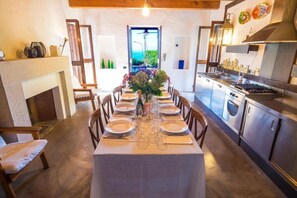 A dining area with a table set for six, a fireplace, and a kitchen with stainless steel appliances. - Villa Dilù (Maratea)