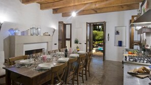 Zona pranzo con tavolo in legno apparecchiato per sei persone, camino e vista sul giardino.