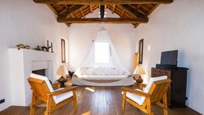 A room with a bed, two wooden chairs, a fireplace, and a television.