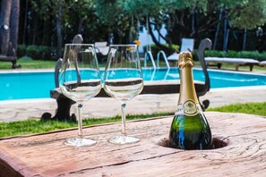 Et træbord med to tomme vinglas og en champagneflaske foran en swimmingpool.