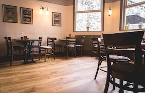 A dining area with wooden chairs and tables, framed motorcycle pictures on the wall, and a window with a view of buildings.