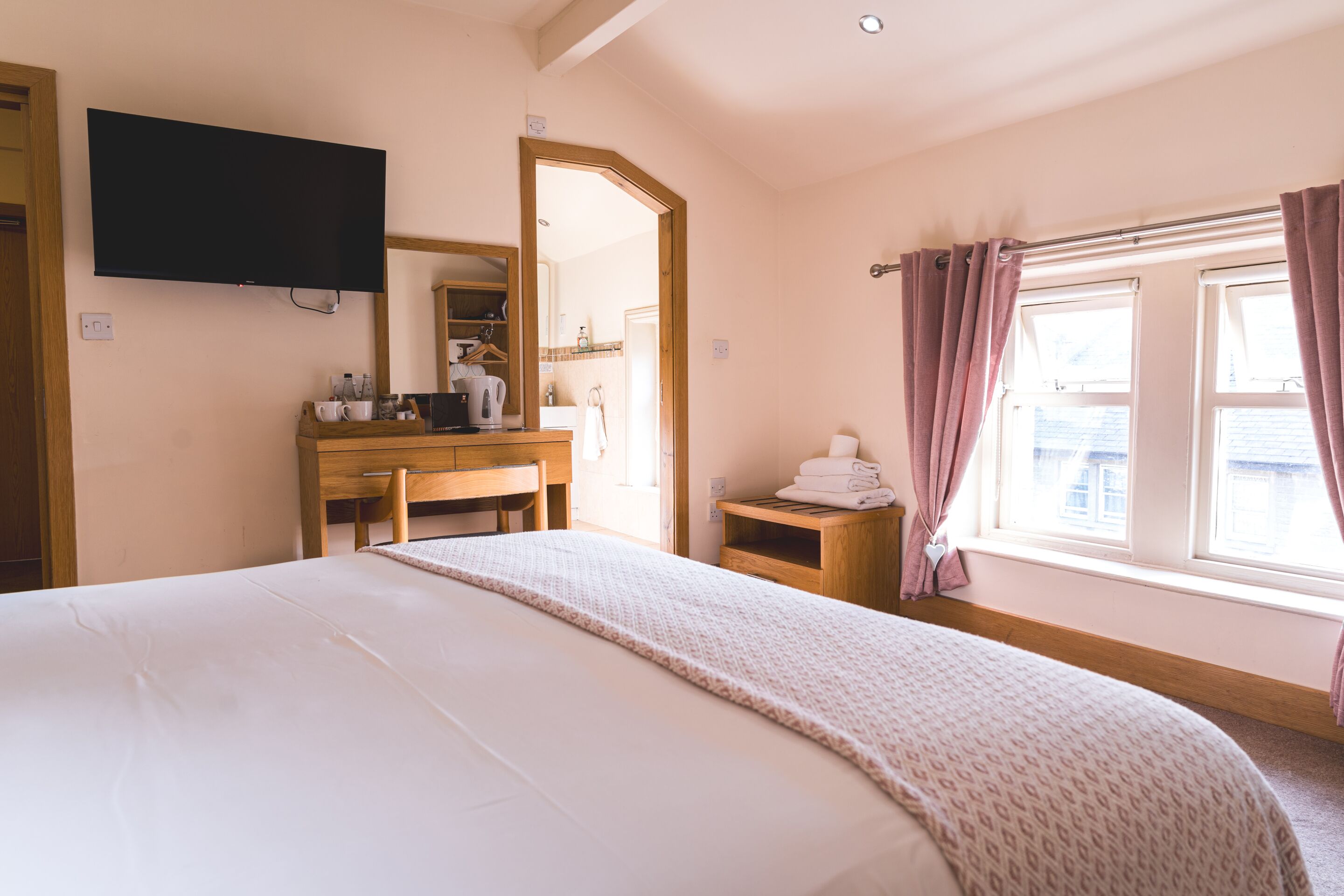 Une chambre à coucher comprenant un lit, un bureau, un miroir, une télévision et une fenêtre avec des rideaux.