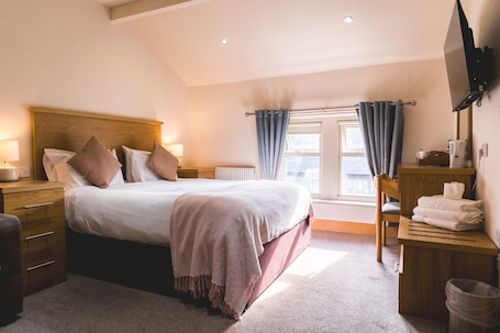 A bedroom with a bed, bedside tables, a wooden dresser, a TV, and a window with curtains.