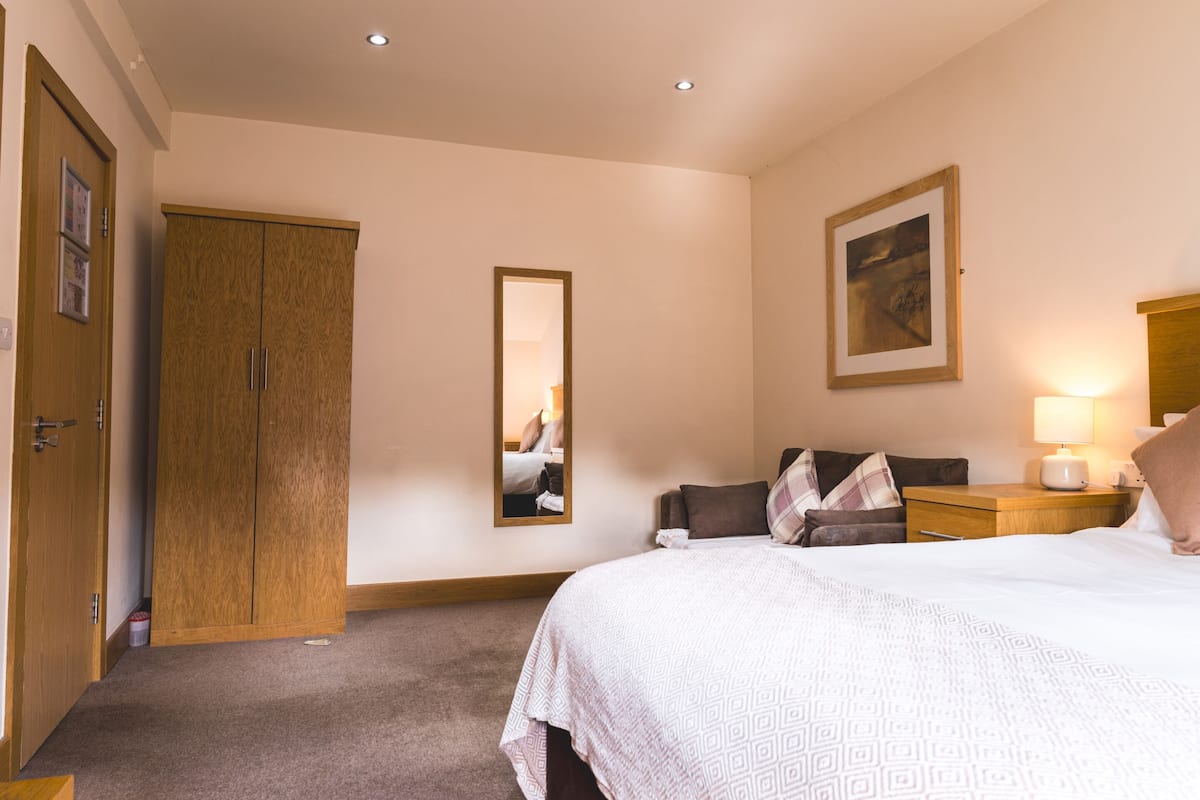 A bedroom with a bed, a wardrobe, a mirror, a nightstand, and a lamp.