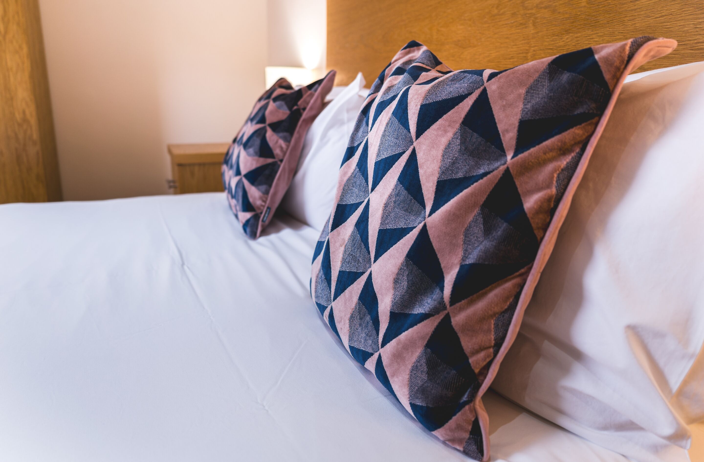 A neatly made bed with patterned pillows and a wooden headboard.