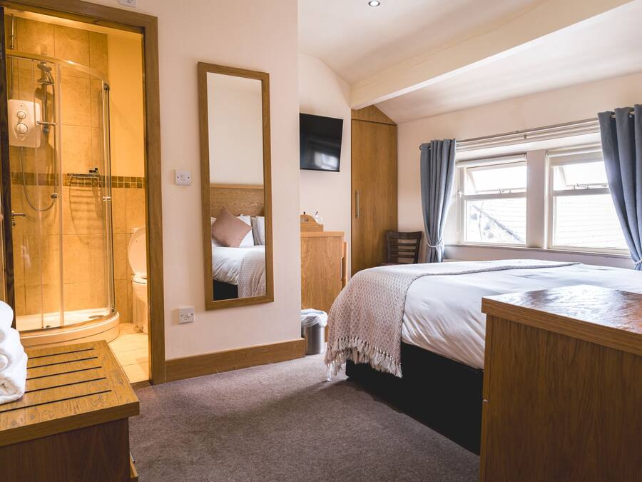 A hotel room with a shower, a bed, a wooden desk, a mirror, and a TV.