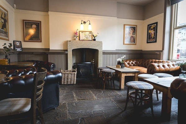 A cozy pub with leather seating, a fireplace, and various framed pictures on the walls.