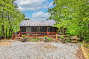 A cabin with a wooden deck, surrounded by trees, and a gravel driveway. - Dog-friendly steps to Warwoman Dell in the Chattahoochee National Forest (Clayton)