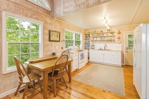 A kitchen with wooden flooring, white cabinets, a dining table with chairs, and a large window. - Dog-friendly steps to Warwoman Dell in the Chattahoochee National Forest (Clayton)