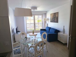 Un salon moderne avec un canapé bleu, une table à manger en verre entourée de chaises, une lampe blanche et un tableau accroché au mur.