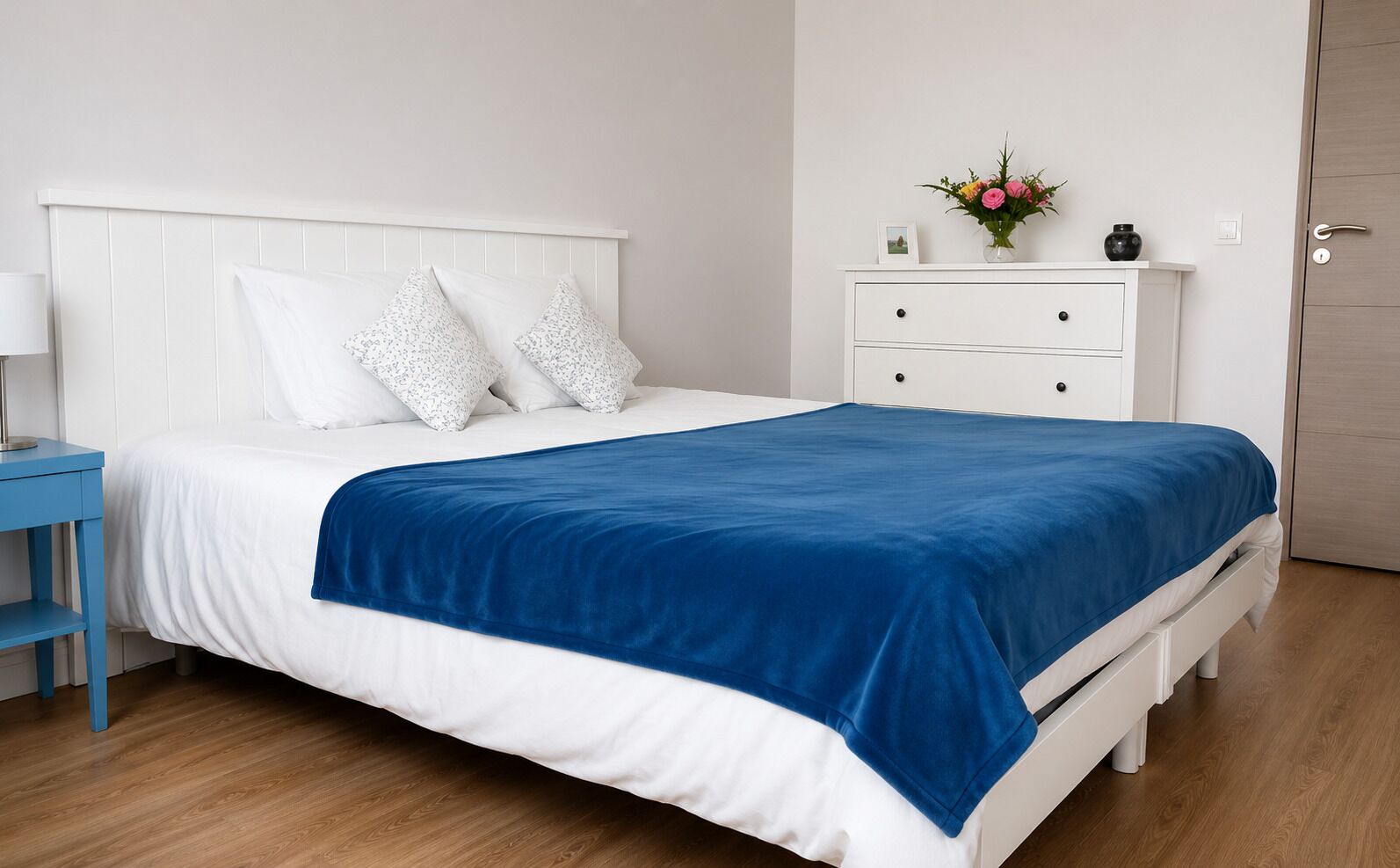 A neatly made bed with a blue blanket, white pillows, and a white headboard.