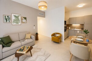 Un salon moderne comprenant un canapé, un fauteuil, une table basse et un coin repas avec une table mise pour deux personnes.