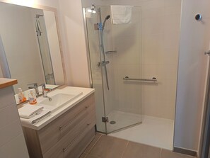 Et moderne badeværelse med en glasafskærmet brusekabine, et spejl og en vaskebord.