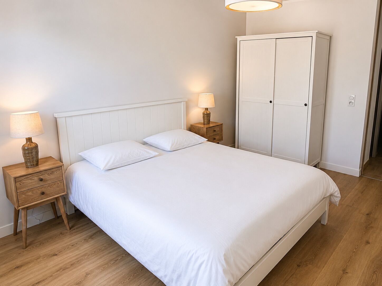 A bedroom with a bed, two bedside tables, a wardrobe, and a lamp on each table.