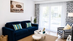 Uma sala de estar com um sofá azul escuro, almofadas listradas, uma mesa de centro branca e poltronas listradas.