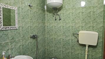 Un baño con baldosas de mármol verde, un lavamanos pedestal, un bidé, un inodoro y un calentador de pared.