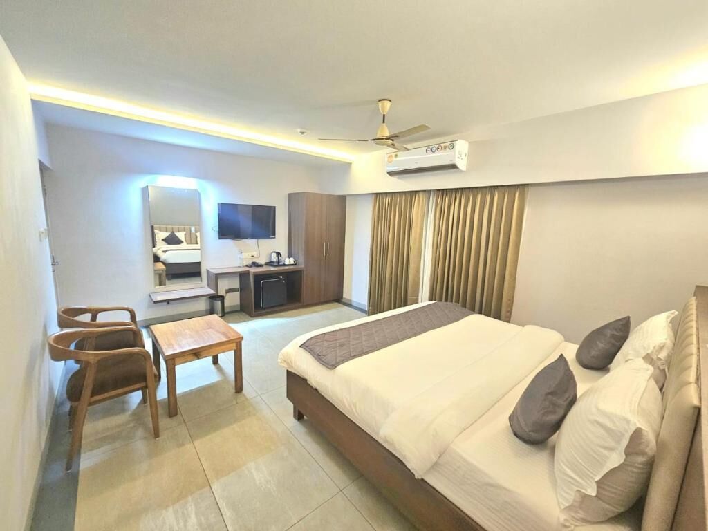 A hotel room with a bed, a desk, a chair, a television, and an air conditioning unit.