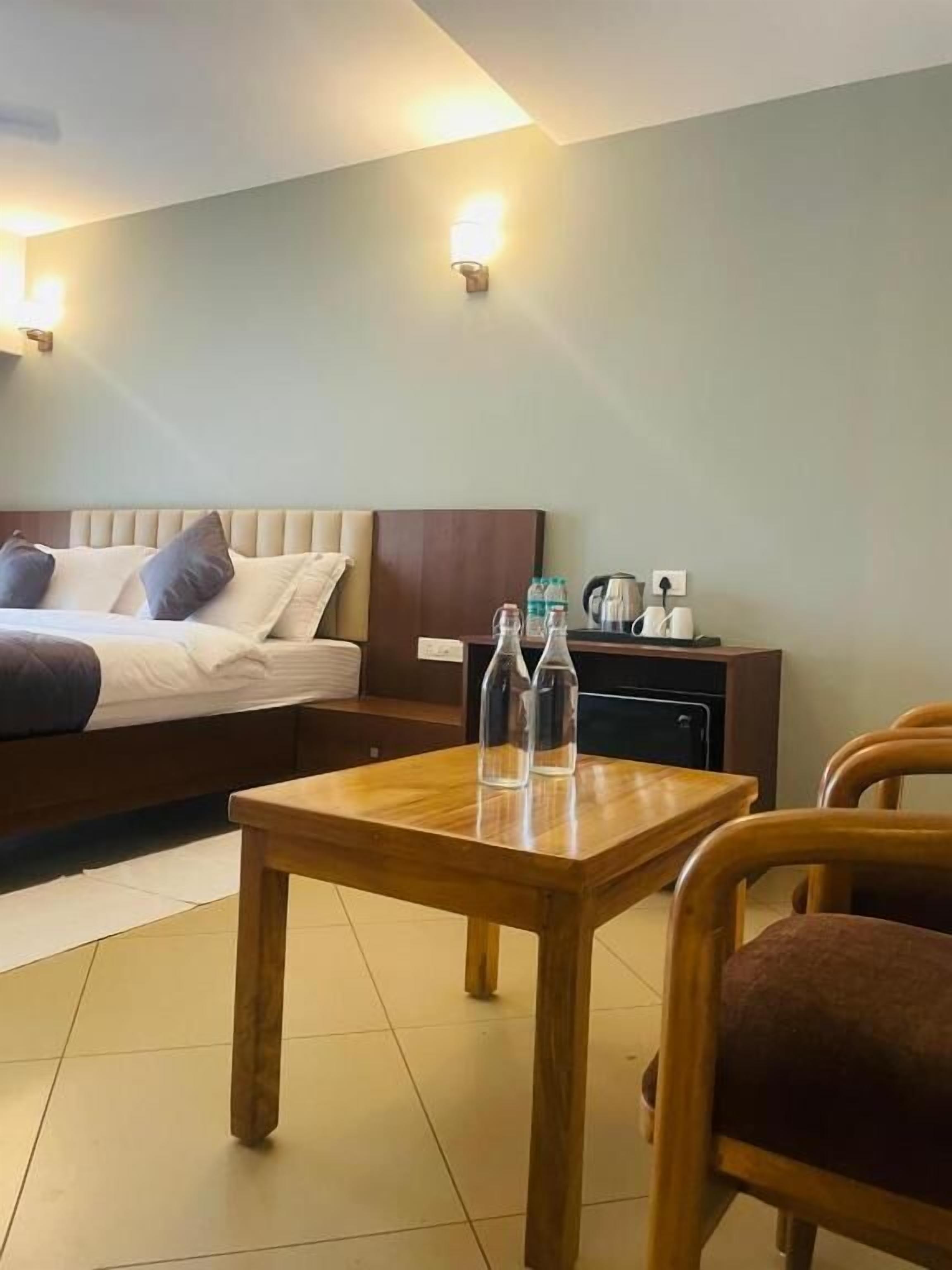 A hotel room with a bed, a wooden table, two chairs, a nightstand, and wall-mounted lights.