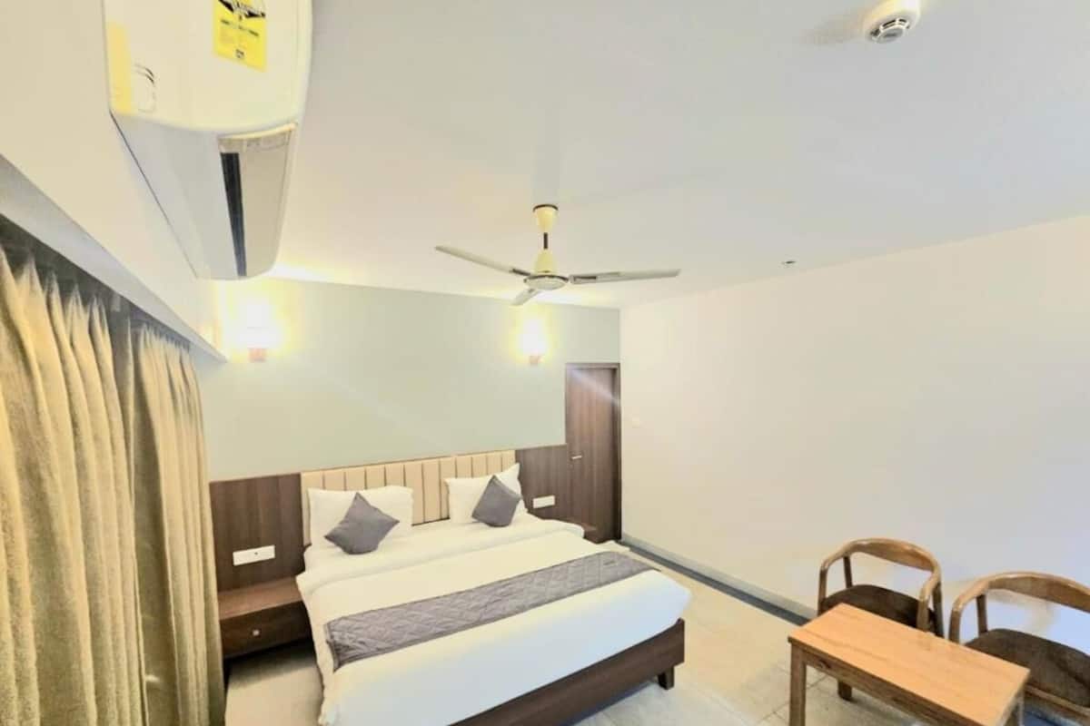 A hotel room with a bed, a desk, two chairs, a ceiling fan, and a wall-mounted air conditioner.