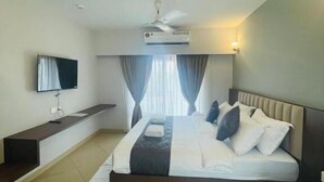 Quarto de hotel moderno com cama, televisão de tela plana, ventoinha no teto e ar condicionado.