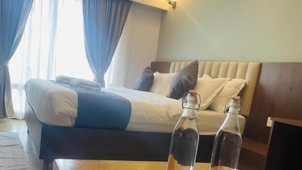 Quarto de hotel com cama, mesa de madeira com duas garrafas e ar condicionado fixado na parede.