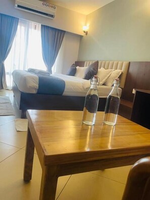 Una habitación de hotel con cama, una mesa de madera con dos botellas y un aire acondicionado de pared.