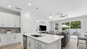 A modern kitchen with white cabinetry, a central island, and a dining area with a gray sofa and chairs. - Beautiful 3BR 3BA Townhome~ Steps from the Beach! (Fernandina Beach)