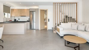 Een moderne keuken met een centraal eiland, een zithoek met een witte bank en een kleine tafel, en een trap naar een entresol.