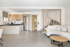 Eine moderne Küche mit einer zentralen Kochinsel, ein Essbereich mit einem weißen Sofa und einem kleinen Tisch sowie eine Treppe, die zu einem erhöhten Bereich führt.
