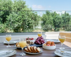 Ein Tisch mit Frühstücksangeboten, darunter Obst, Brot und Getränke, vor einer Baumlandschaft und blauem Himmel.